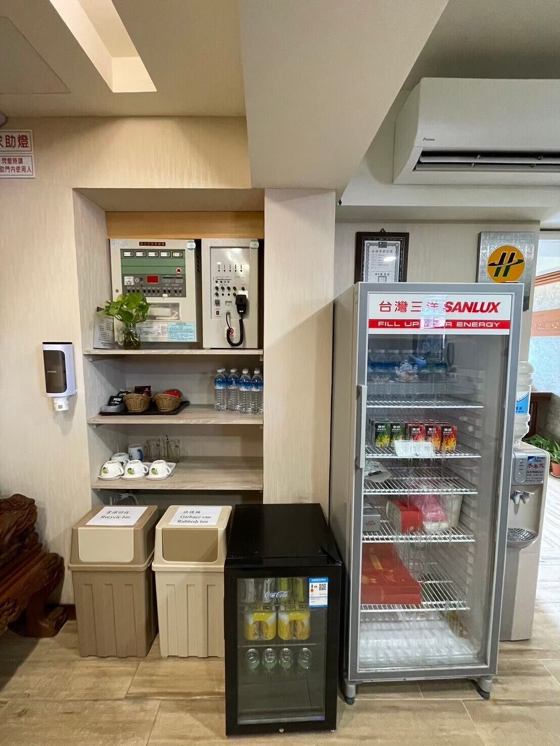 琉戀客佔飯店：公共補給角有飲料冷藏櫃、飲水機、茶杯架、分類垃圾桶與牆上電話設備。