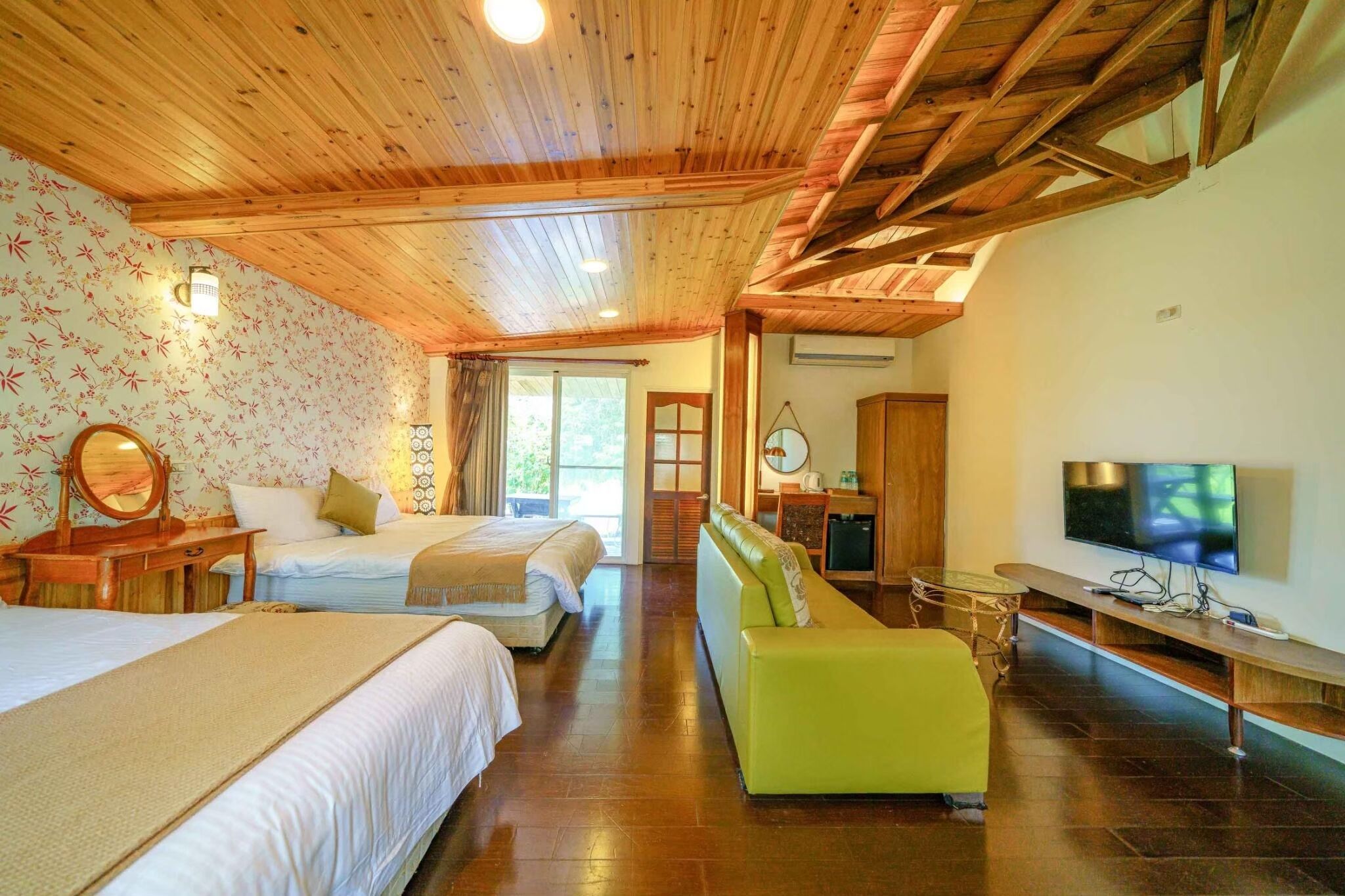 芳草古樹木屋頂客房的兩張床、綠色沙發、木鏡台與壁掛電視。