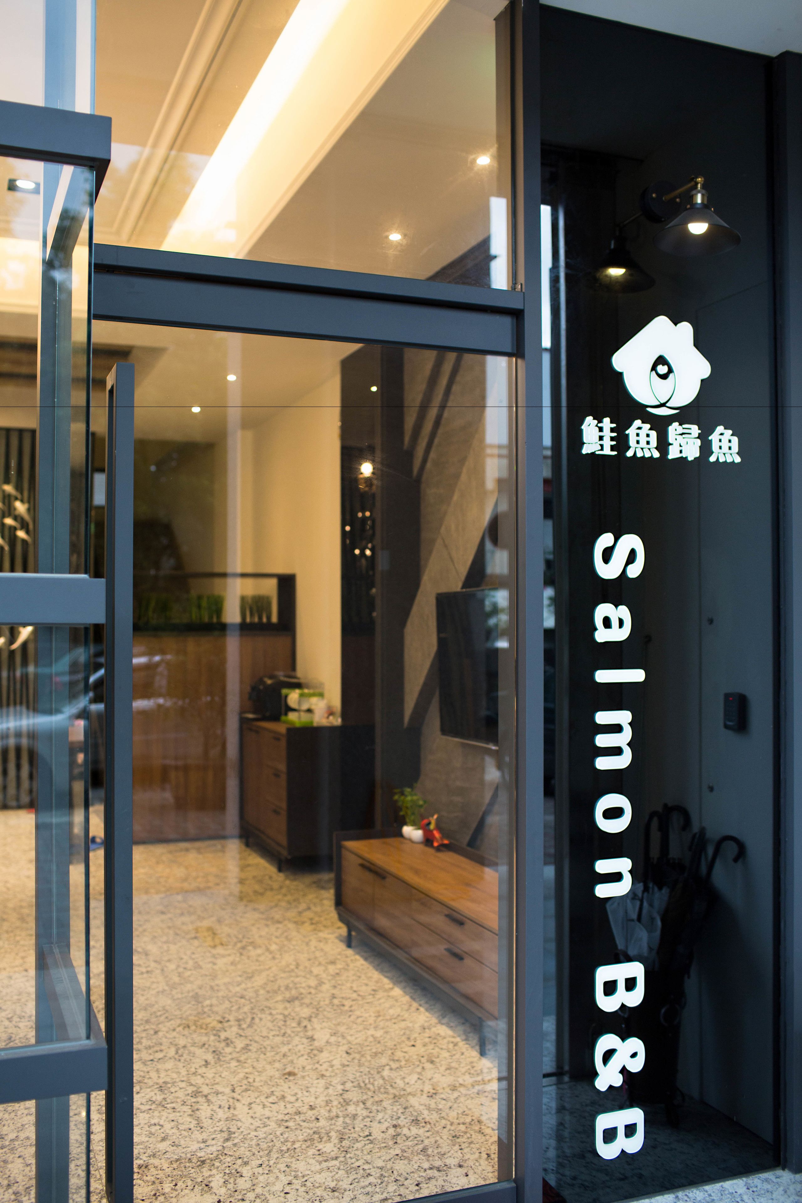 鮭魚歸魚民宿入口，深色立面上有白色魚形標誌與直排的 Salmon B&B 招牌。