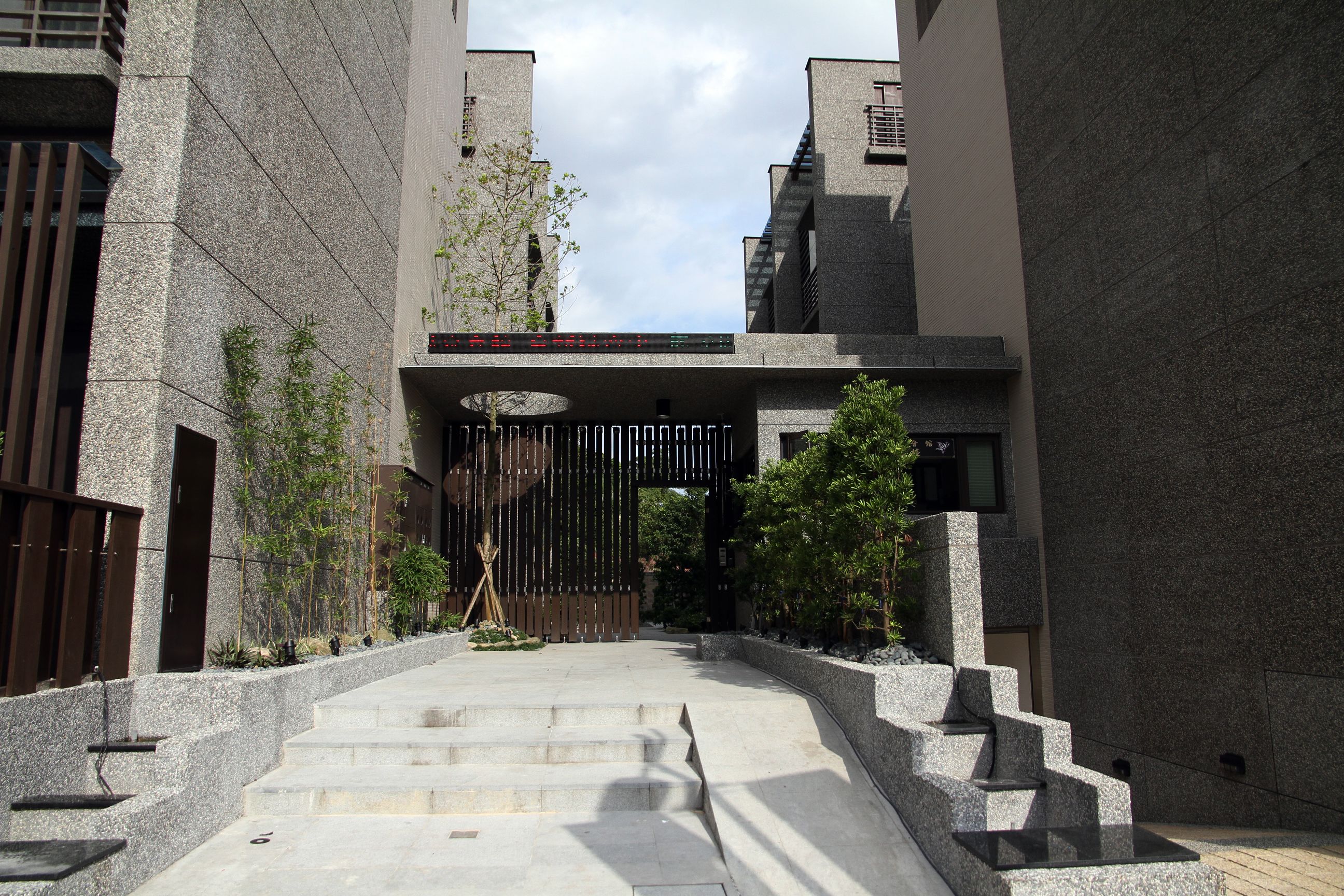 靜界溫泉會館：灰色建築之間的入口石階、木格柵大門與兩側植栽。