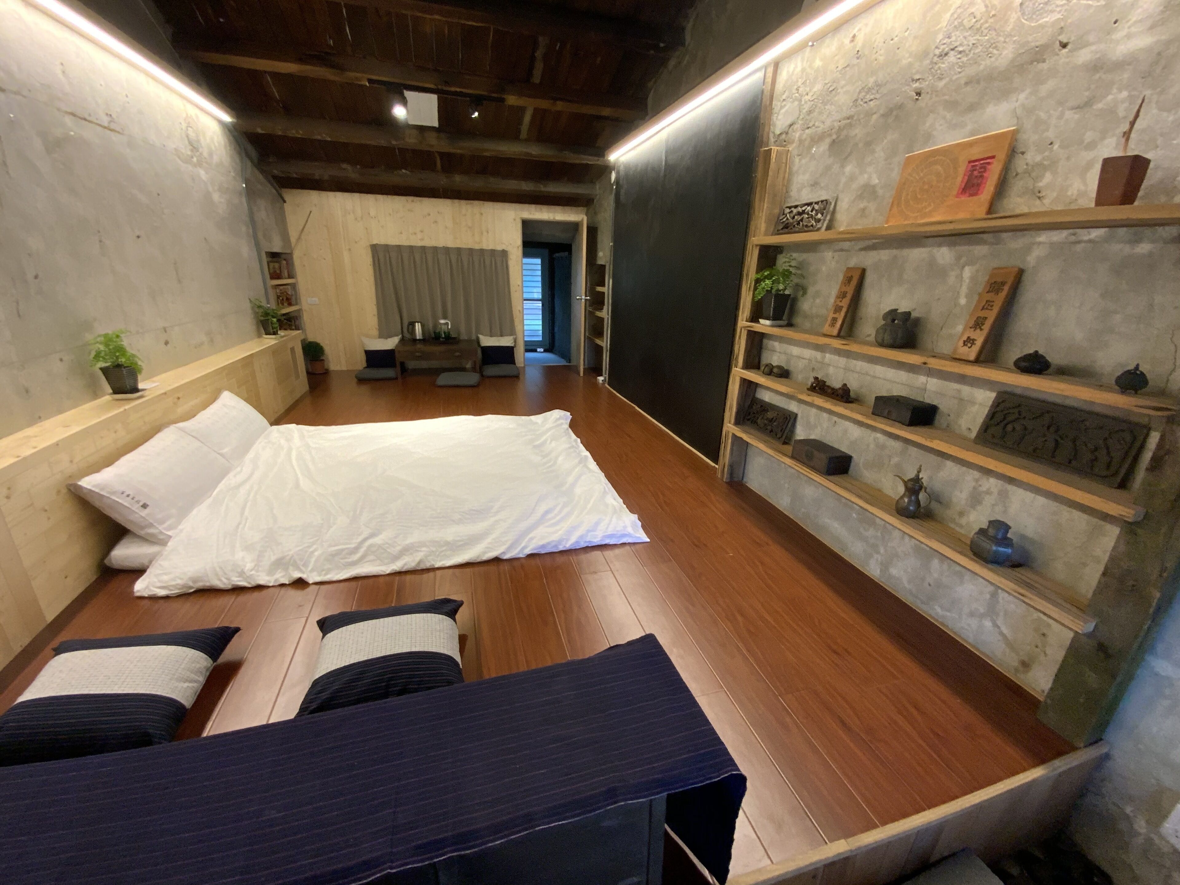 古意生活藝術館客房的白色床墊、木地板、坐墊低桌與牆邊展示架。