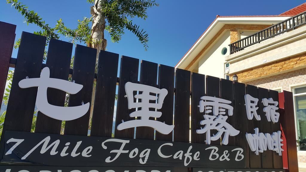 七里霧民宿：黑色木柵上的白色七里霧民宿招牌，後方是淺色外牆與陽台。