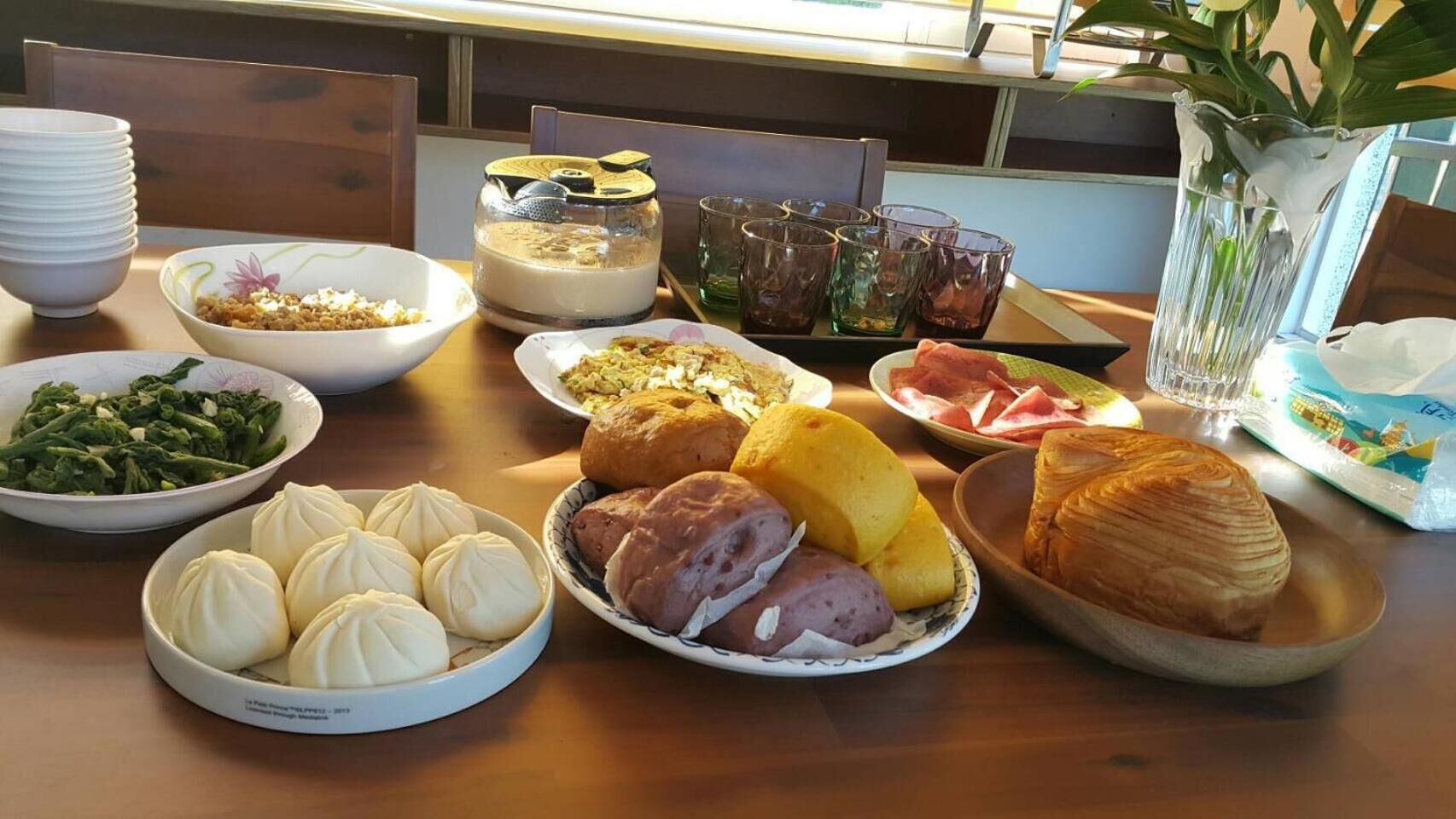 七里霧民宿：木桌上有包子、饅頭、麵包、蛋料理、青菜、火龍果與飲品。